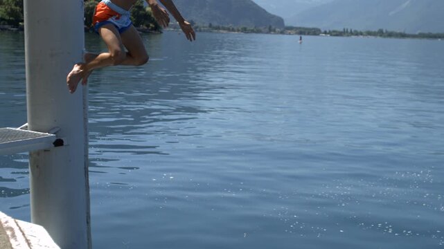 Boy suspended above lake slow motion, curled into cannonball position mid-jump, playful summer moment filled with excitement, adventure, and fun