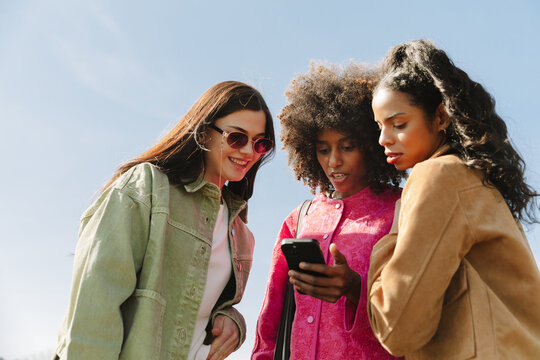 A group of three female friends standing and looking at a phone that one of them is holding while one of them is smiling
