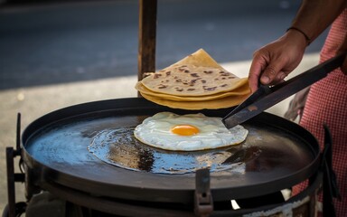 Street vendor cooking a fried egg and stacking crepes on a hot griddle outdoors