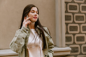 A woman is talking on the phone and standing by the wall