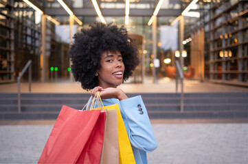 Happy businesswoman holding shopping bags is turning around near mall entrance