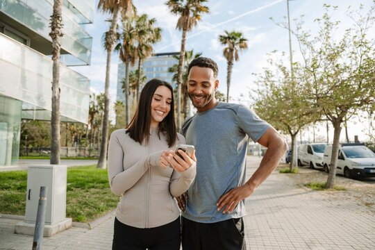 A man looks at a phone held by a woman standing next to him while they smile