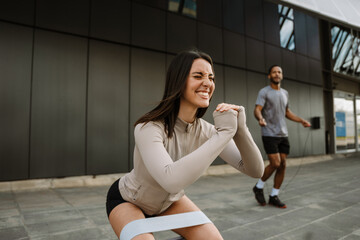 A female athlete squats with her eyes closed and her hands together while a rubber band is on her...