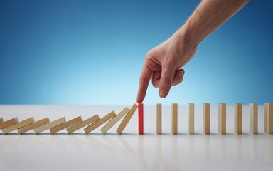 Finger stopping domino effect with one red domino in the middle, symbolizing risk management and strategy