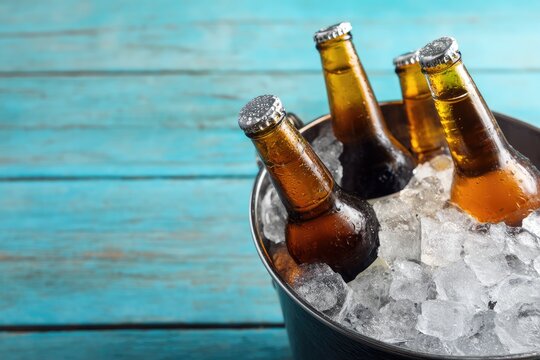 Cold beer bottles in bucket filled with ice on turquoise wooden table, perfect for summer bar ads, beach party invitations, brewery promotions, and festive drink marketing