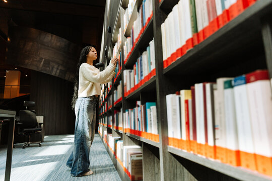 A female student chooses a book on a bookshelf - Powered by Adobe