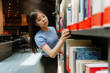 A female student takes one of the books off the bookshelf