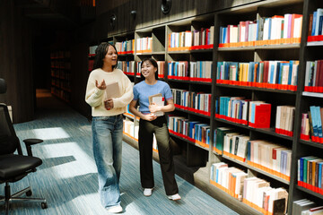 Two female students talking and smiling while holding books and walking