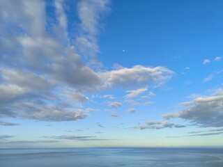 Serene blue sky with fluffy clouds over calm ocean waters  