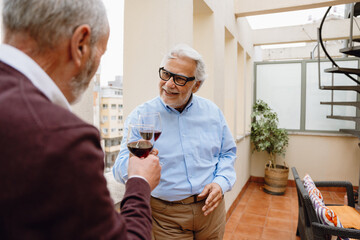 A man smiles and looks at a male friend while they hold glasses