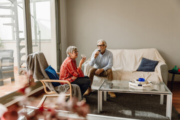 A man sits on a couch next to a woman sitting in a chair while they hold glasses