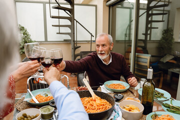 A man sits at a table clinking glasses with a group of three friends next to him