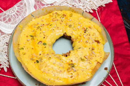 Beautiful round malai Ghevar, famous sweet or Rajasthan India, serve on a red background. Ghewar having creamy yellow topping with nuts.