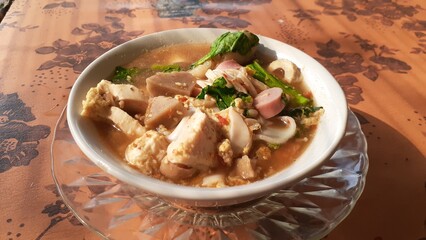 A bowl of Seblak on the table. A typical West Javanese dish. Made with crackers, galangal, garlic, eggs, vegetables, meatballs, sausage, and chicken feet. Wet Seblak. Soup Seblak.