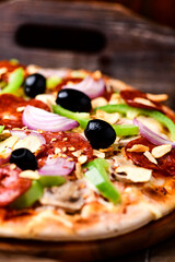 Pizza with chorizo ​​sausage, mozzarella cheese, green pepper and black olives. Rustic wooden background. Soft focus.	