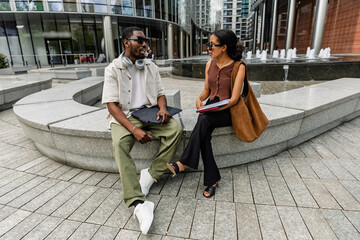 Male and female workers sitting on a bench and talking while holding folders