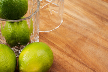 Fresh limes rest near a glass on a wooden table, ideal for crafting cocktails or beverages during a...