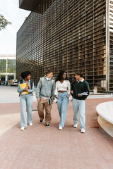 A male student walks and talks to a group of three classmates while they smile