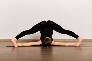 Yoga practitioner executes challenging forward bend on mat in serene studio. Wooden floor and...