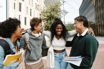 A group of four students hug and laugh while holding notebooks
