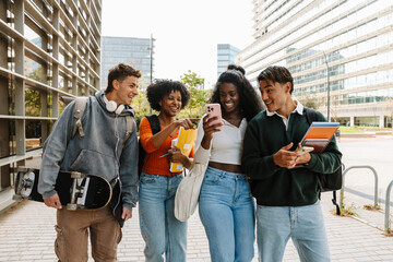 A group of four students laugh and are surprised while looking at a phone that one of them is holding