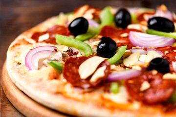 Pizza with chorizo ​​sausage, mozzarella cheese, green pepper and black olives. Rustic wooden background. Soft focus.	
