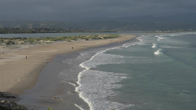 A stunning 4K 30fps video of Lookout Beach, Plettenberg Bay, Western Cape, South Africa, showcasing dramatic waves, golden sand, lush greenery, and moody sunset skies along a breathtaking coastline.