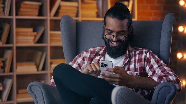 Smiling Indian student scrolling social media in library, using dating app