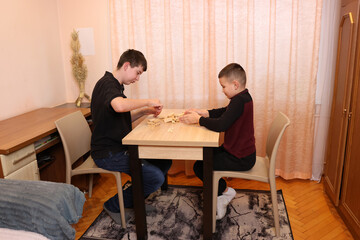 Fototapeta premium Two boys are sitting at a table assembling a wooden game together, focused and smiling.