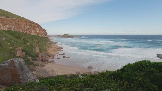 Breathtaking 4K 30fps video of Robberg Nature Reserve, Plettenberg Bay, Garden Route, South Africa. Rugged cliffs meet the Indian Ocean under a vivid blue sky with streaking clouds, showcasing nature.