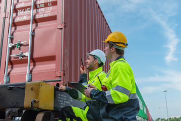 Efficient workers in safety gear inspect cargo containers on railway track, ensuring proper handling and safety protocols are followed. Their teamwork highlights importance of safety in logistics
