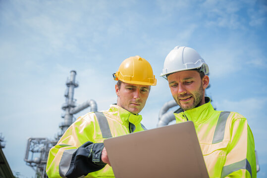 Construction workers in safety gear examine tablet outdoors, showcasing teamwork and collaboration in industrial setting. Their bright jackets and helmets highlight safety in workplace