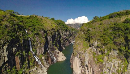 Aerial view of waterfalls cascading down rocky cliffs into a valley. Lush greenery covers the surrounding mountains
