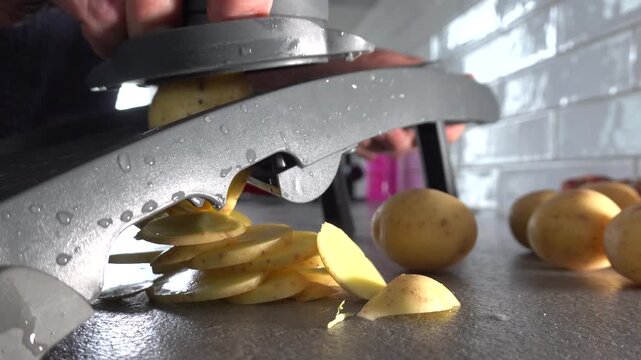 Stockholm, Sweden A cook in a home kitchen uses a mandolin slicing machine to slice potatoes into even slices. 