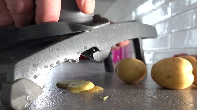 Stockholm, Sweden A cook in a home kitchen uses a mandolin slicing machine to slice potatoes into even slices. 