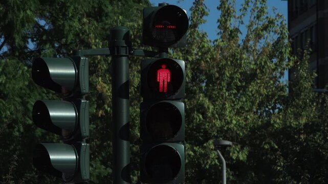Red pedestrian signal shows a walking man, indicating stop for pedestrians. A red silhouette of a walking person illuminated on a pedestrian traffic light, signaling to halt crossing the street