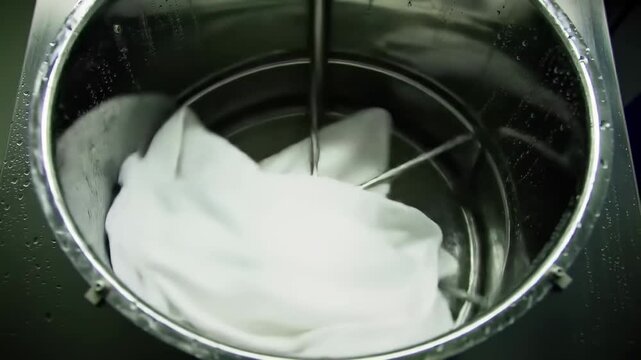 White fabric being processed in a stainless steel industrial dyeing machine at a modern textile factory. Concept of coloration and manufacturing