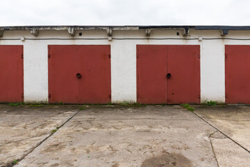 The facade of a low stone garage building. There are several red metal gates and a concrete platform. Background.