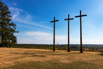 Tall wooden crosses stand on a dry grassy ridge against a clear horizon, evoking Good Friday and Calvary themes. Sparse landscape composition for religion, faith, symbolism, and contemplation