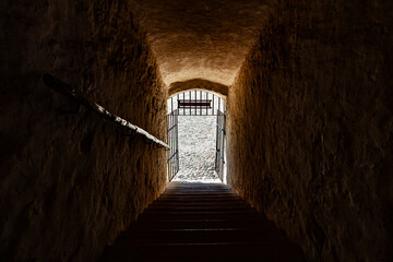 Stone passage with stairs leading to bright iron gate