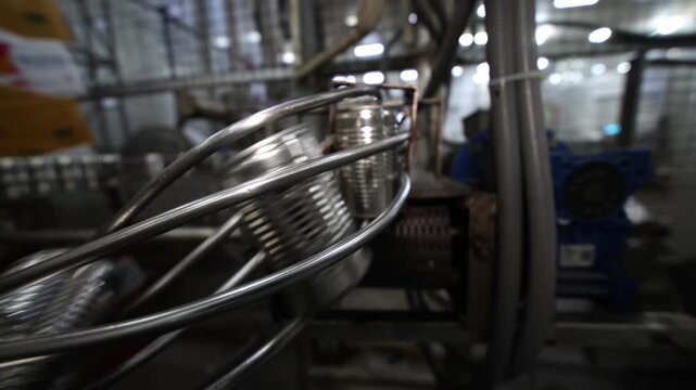 Several metal cans are lined up on a conveyor in a production facility. Workers in the background monitor the machinery's operation, ensuring a smooth flow of the manufacturing process.