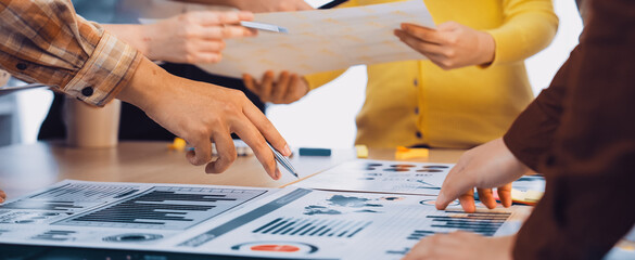 A diverse group of professionals collaboratively analyzing financial charts and reports during a meeting in a bright office setting, showcasing teamwork and engagement. SACTR