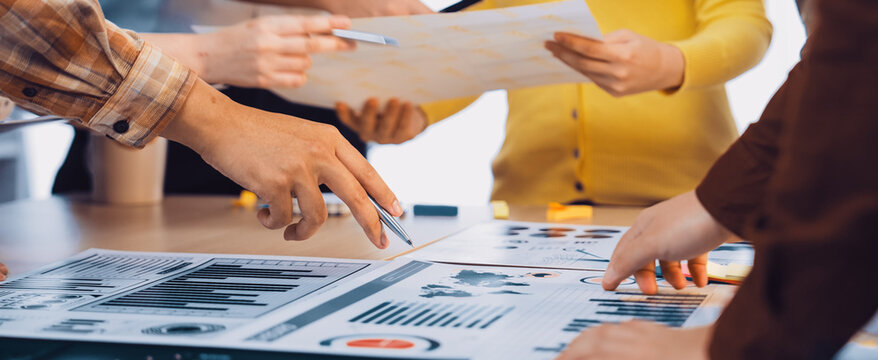 A diverse group of professionals collaboratively analyzing financial charts and reports during a meeting in a bright office setting, showcasing teamwork and engagement. SACTR - Powered by Adobe