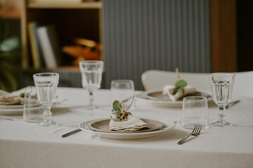 Elegant table setting featuring neatly arranged plates, glasses, cutlery, and folded napkins with decorative greenery on linen tablecloth, prepared for formal dining occasion