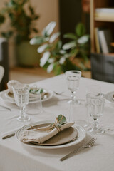 Elegant table setting featuring stacked plates, cloth napkins tied with twine and greenery, clear drinking glasses, forks and knives arranged neatly on tablecloth