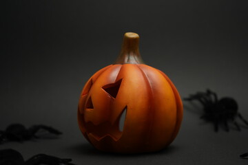 Carved Halloween pumpkin with sinister face surrounded by black spiders on a dark background,...