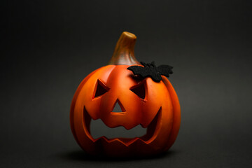 Carved Halloween pumpkin with sinister face and small black bat figure on its side, standing on a...