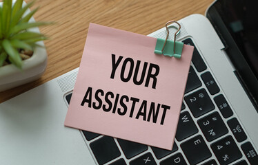 Your Assistant text on a sticker lying on a laptop on an office desk