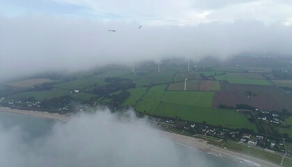 Aerial view of a coastal landscape shrouded in mist, with wind turbines and farmland visible