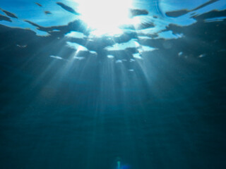 Dark blue ocean surface seen from underwater. Abstract waves underwater and rays of sunlight shining through, Sun light rays undersea deep, Underwater background with sea bottom, Mediterranean sea.